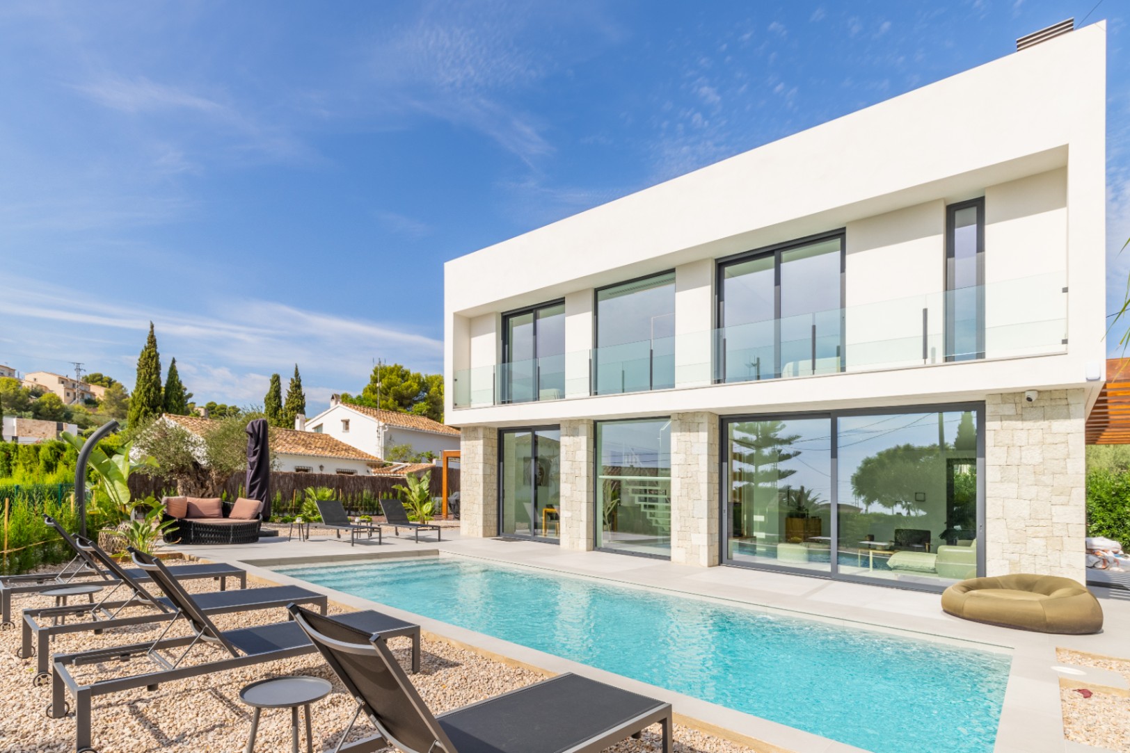 Exterior view of the villa featuring an elongated pool, surrounded by gravel and black sun loungers.