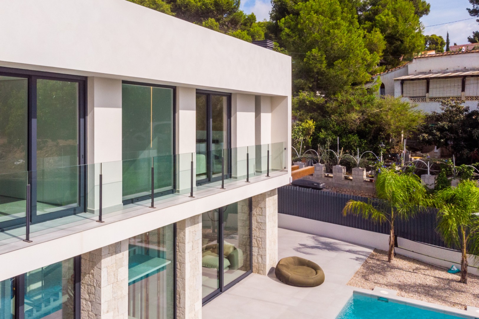 Exterior view of the villa featuring glass balconies, stone cladding, and a turquoise pool.