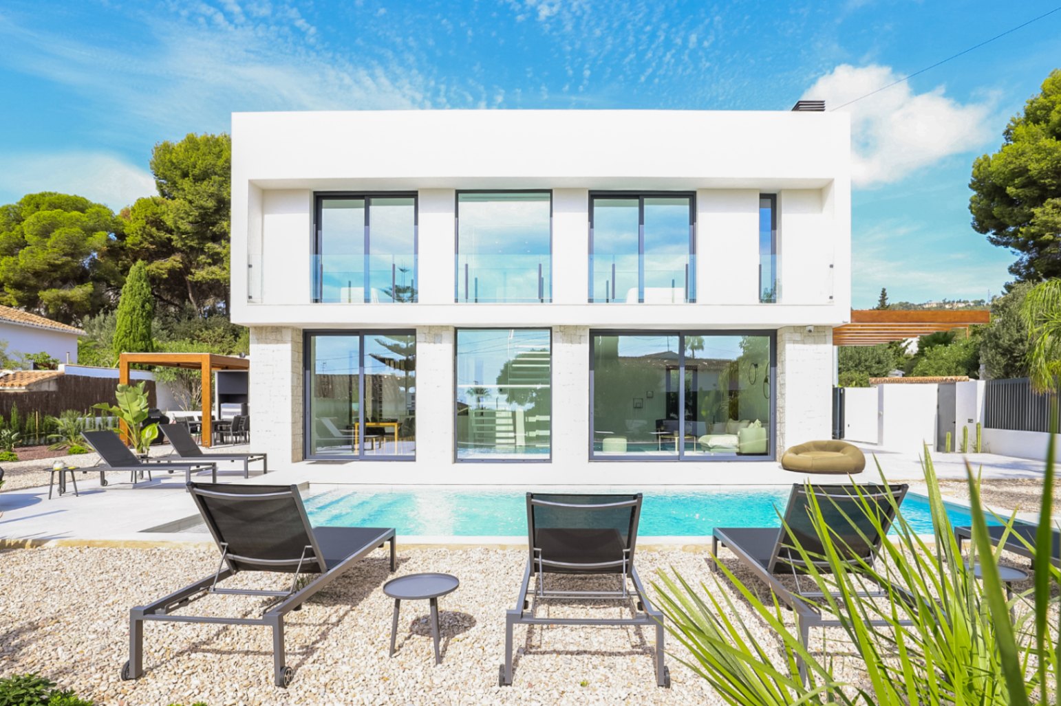 Exterior view of the villa with pool, sun loungers, and a stone facade with large windows.