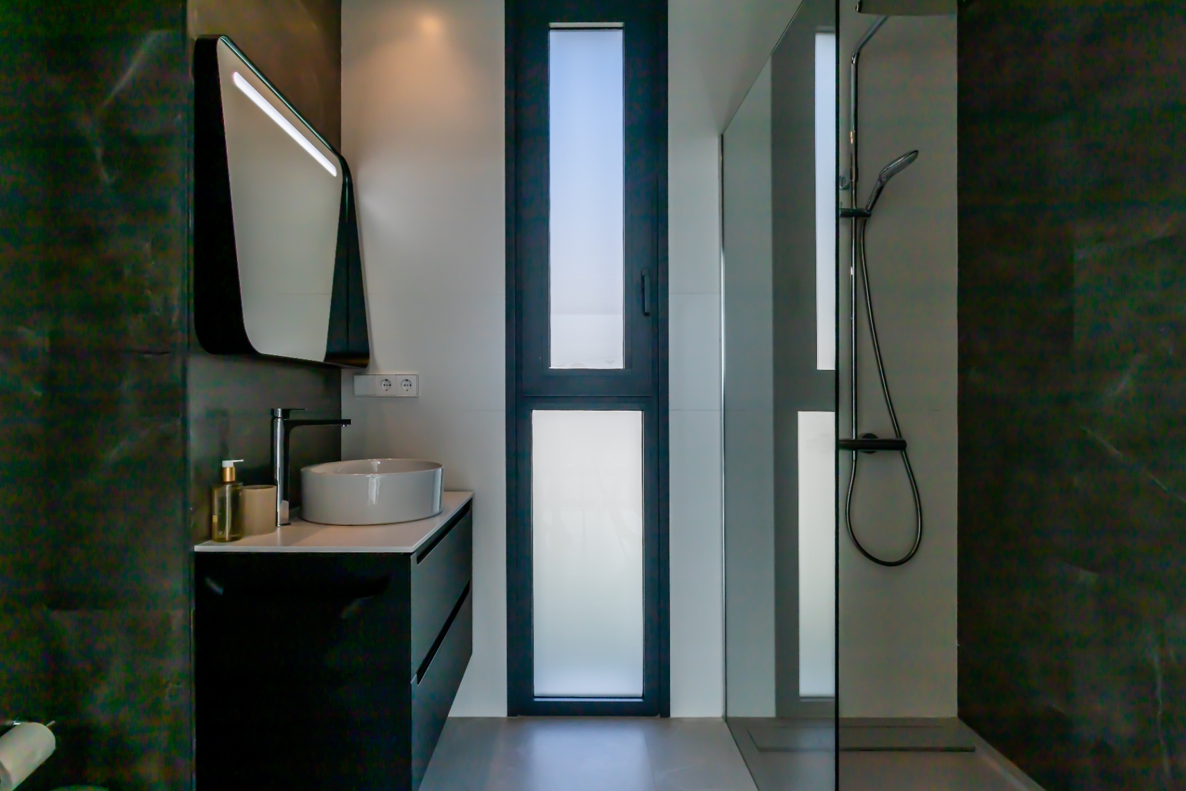 Modern bathroom detail with ceramic sink, black cabinet, and glass-enclosed shower.