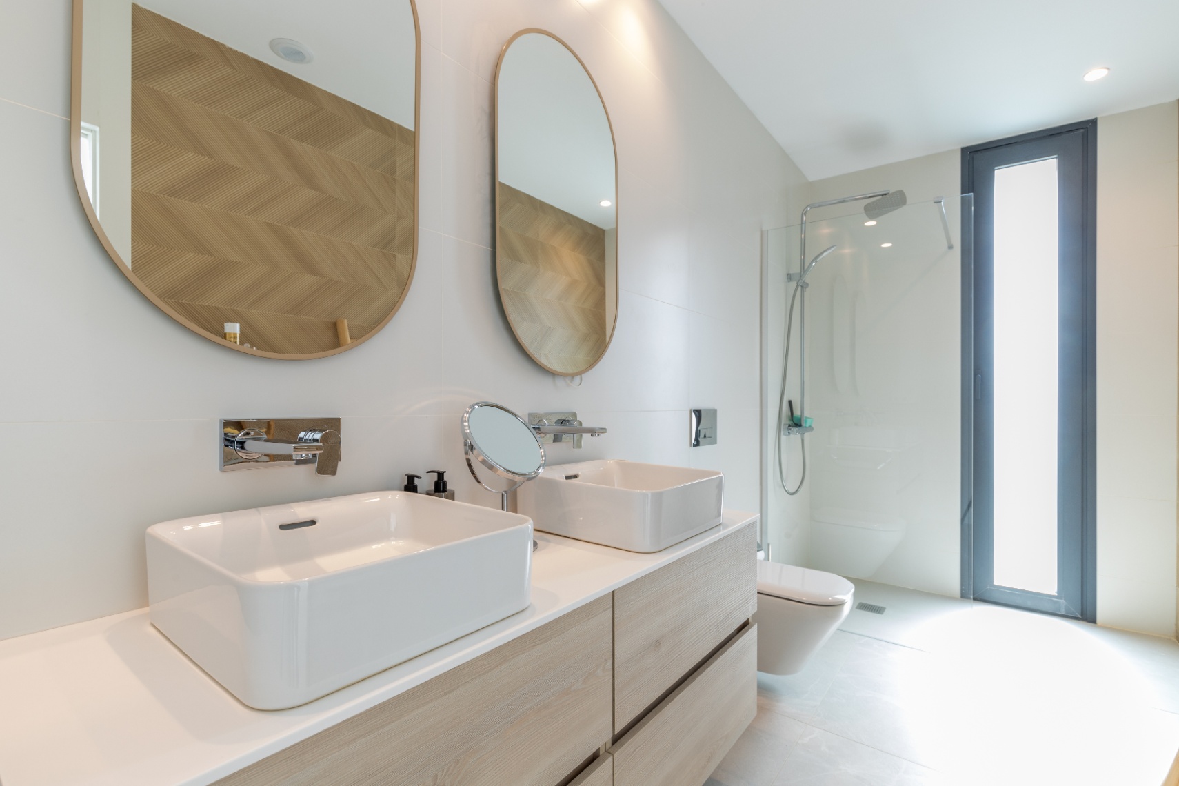 Modern bathroom detail with double sink, oval mirrors, and glass-enclosed shower.