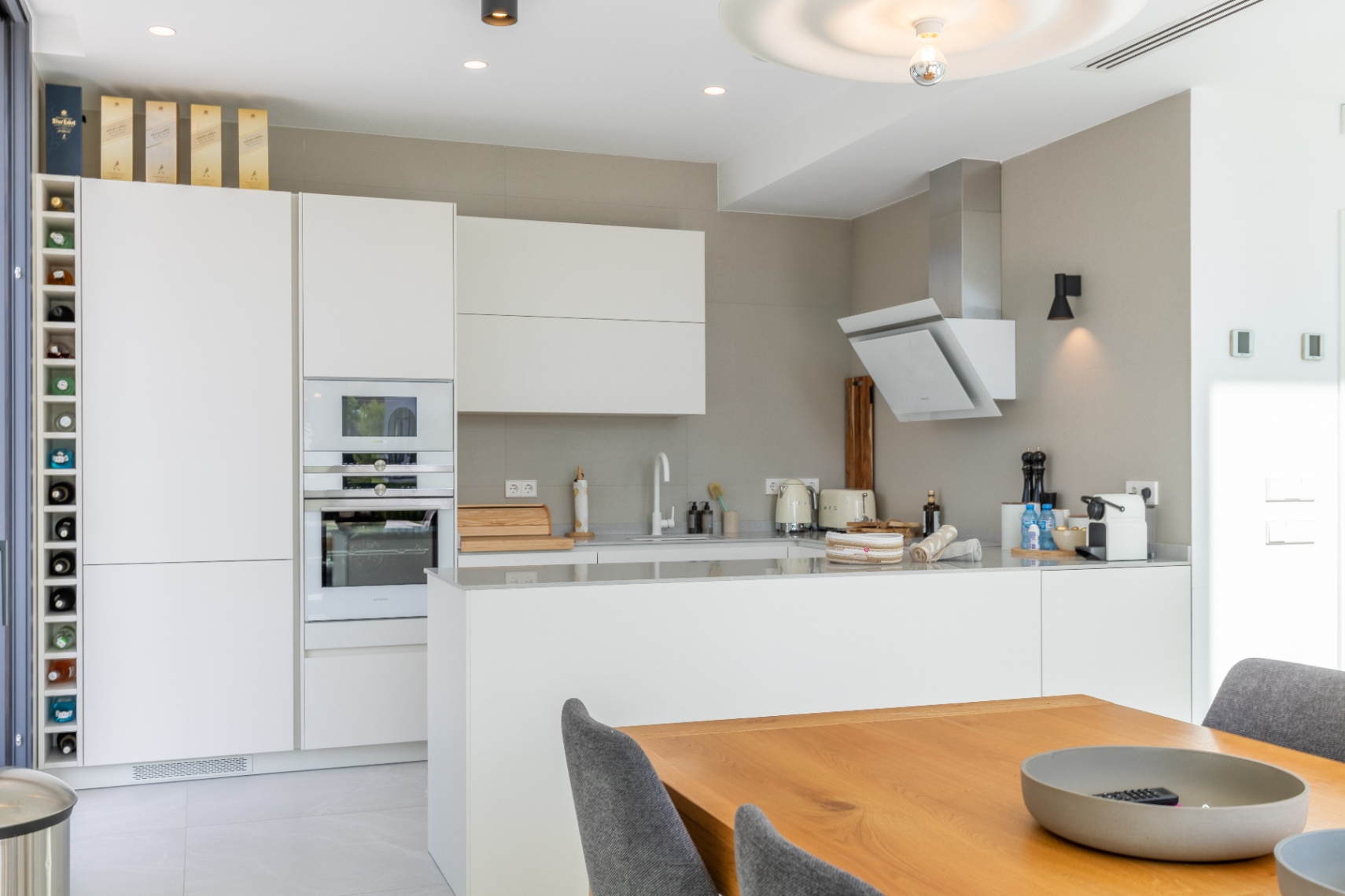 Modern kitchen featuring white cabinets, integrated appliances, and a wooden dining table.