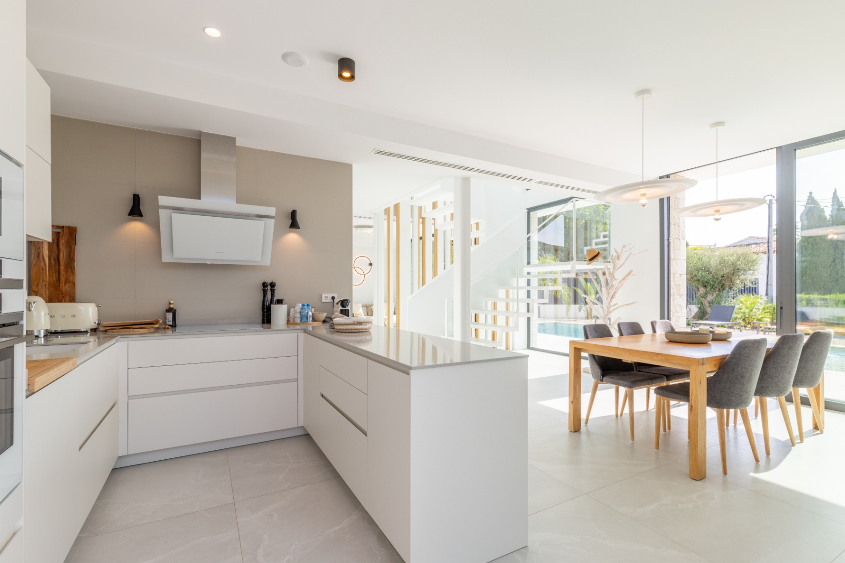 Modern kitchen with central island, light countertops and dining area overlooking the pool.