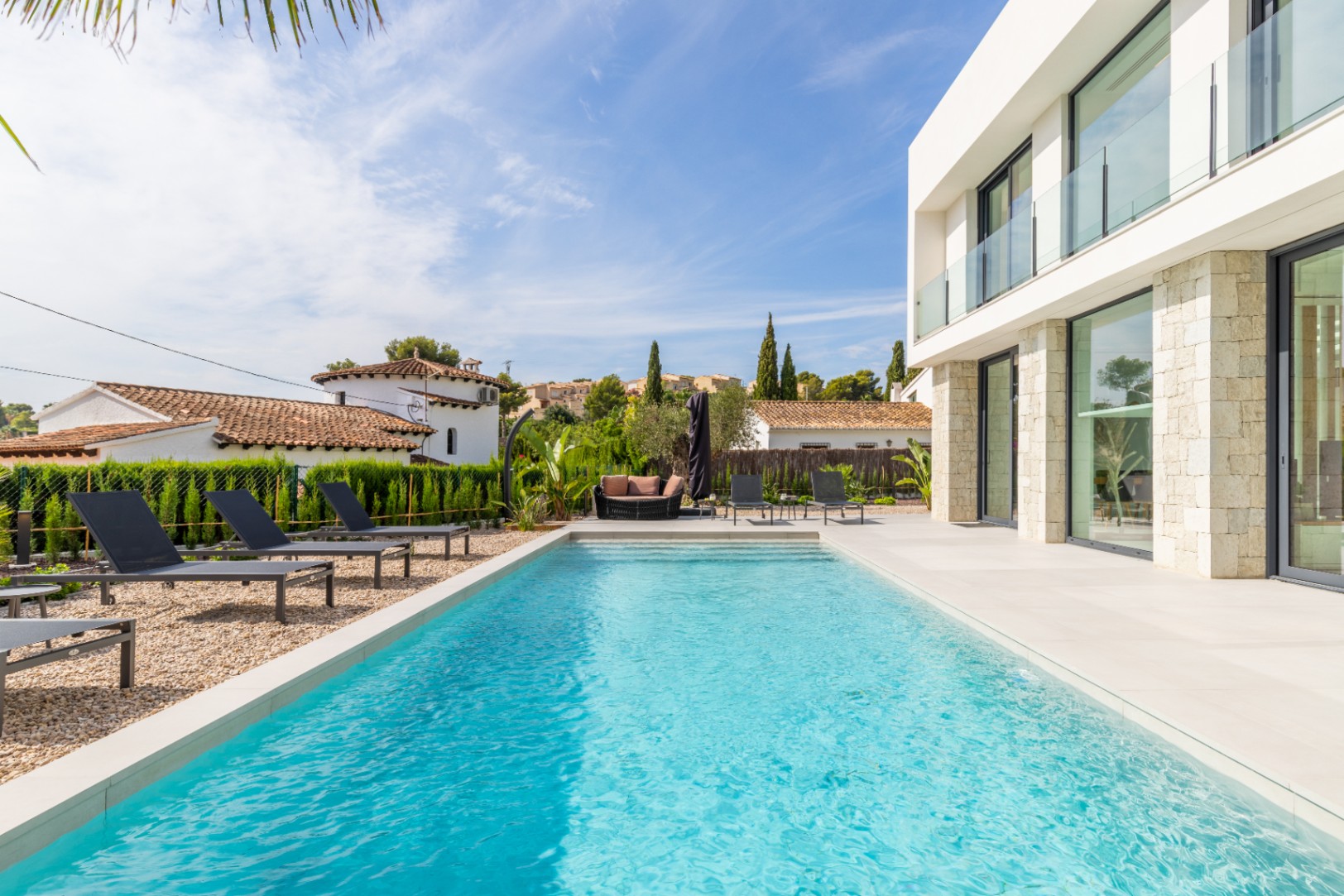 View of the turquoise pool surrounded by sun loungers and the villa's modern stone facade.