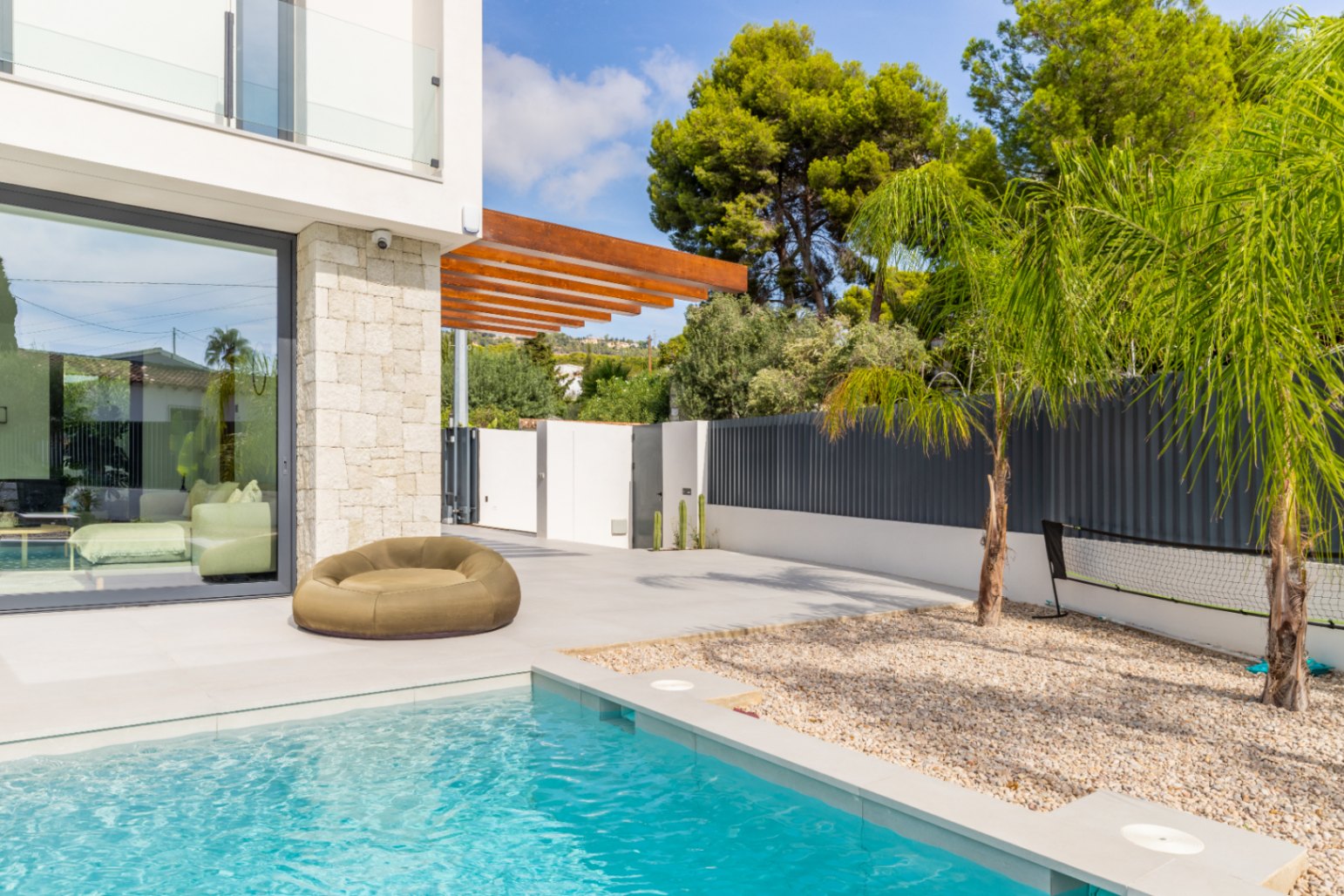 View of the turquoise pool with lounge area and light stone facade in Benissa.
