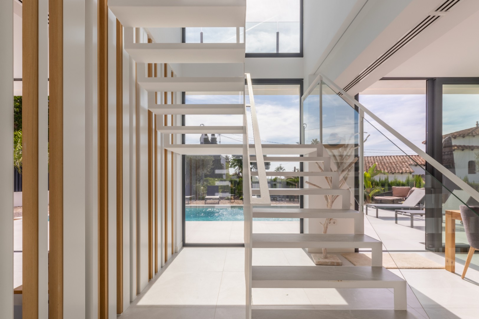 White floating staircase with glass railing and light wood vertical slats.