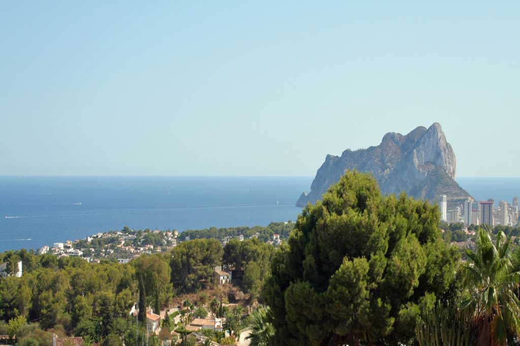 Panoramic views of the Mediterranean Sea and the Peñón de Ifach from the villa's elevated position, framed by a lush canopy of pine trees.