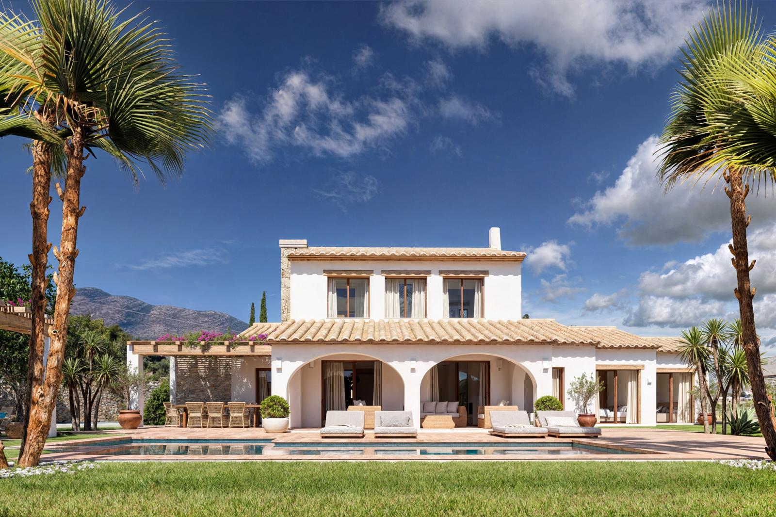 Main facade of the villa featuring arched porches, a rectangular swimming pool, and terracotta sun deck, framed by palm trees and mountain views under a clear sky.