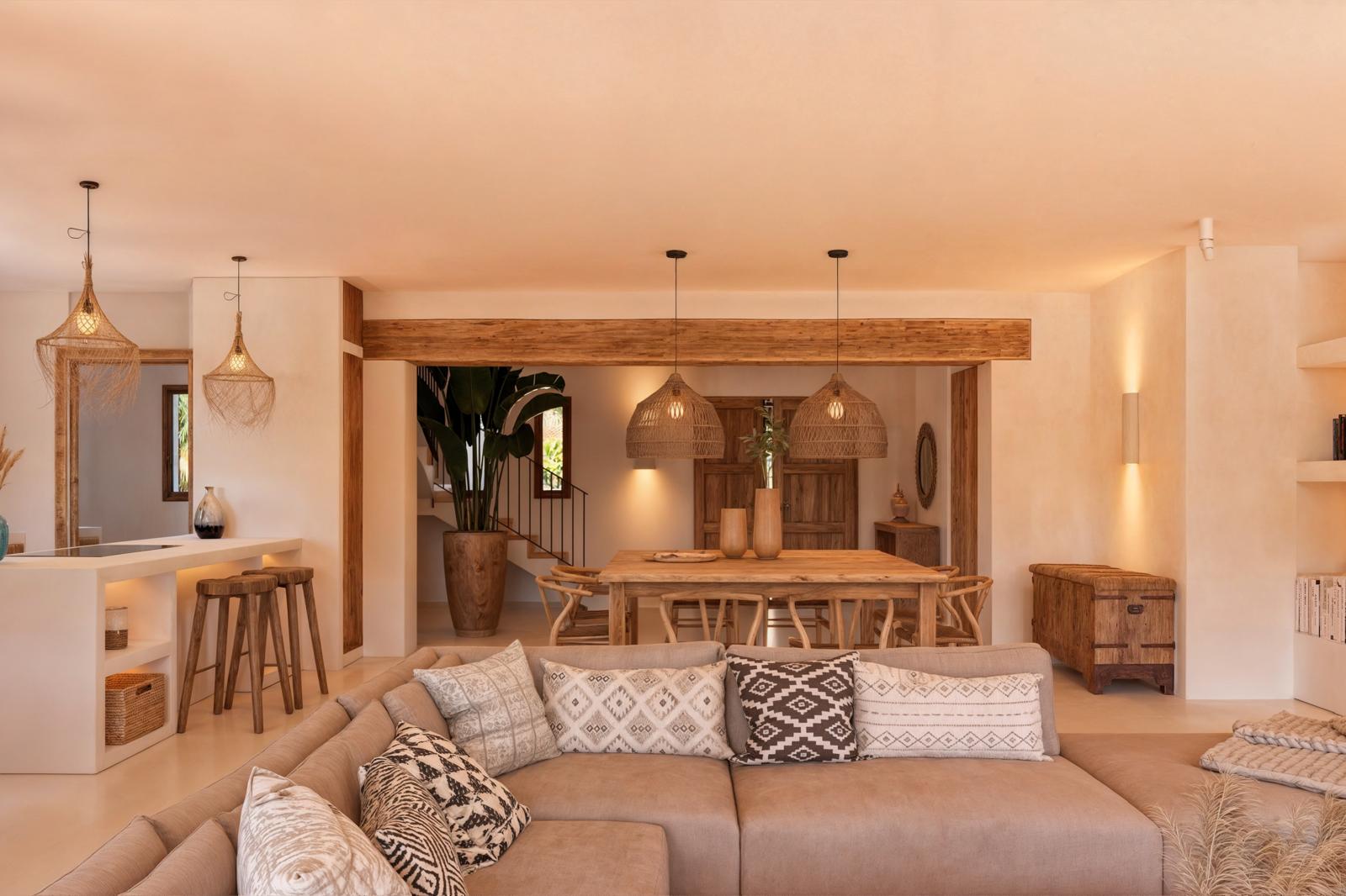 Open-plan living and dining area featuring natural wood beams, woven pendant lighting, and a neutral-toned sofa accented by rustic Mediterranean decor.