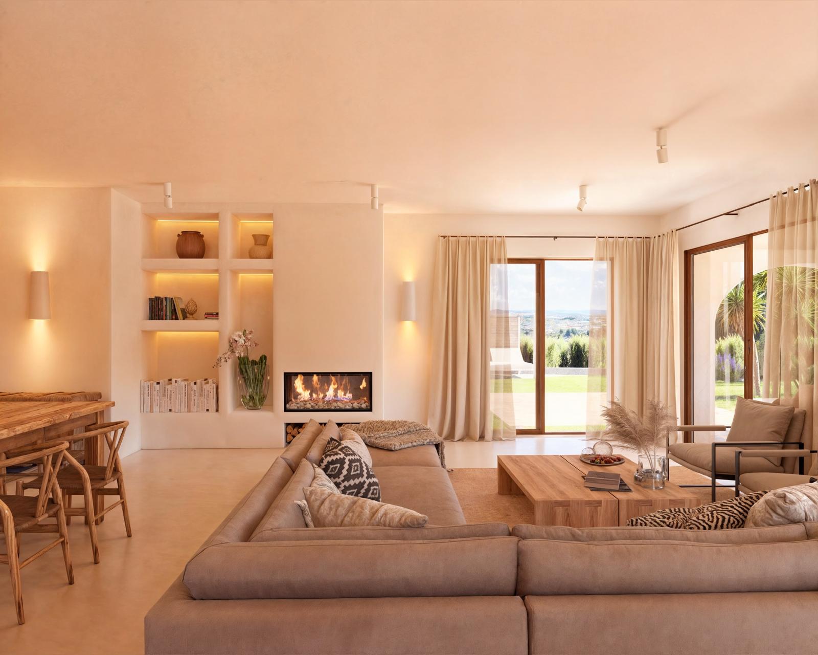 Open-plan living area featuring a built-in fireplace, illuminated shelving, and large Technal glass doors opening to the garden and landscape.