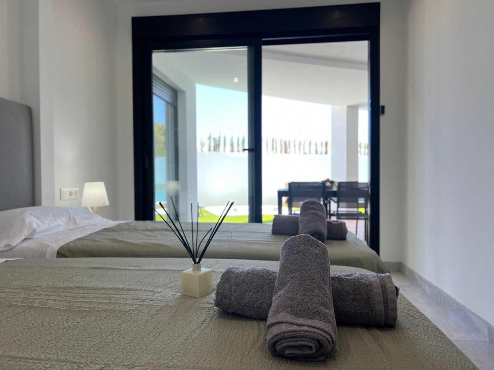 Bedroom featuring twin beds with textured linens and direct access to the outdoor terrace through large black-framed sliding glass doors.
