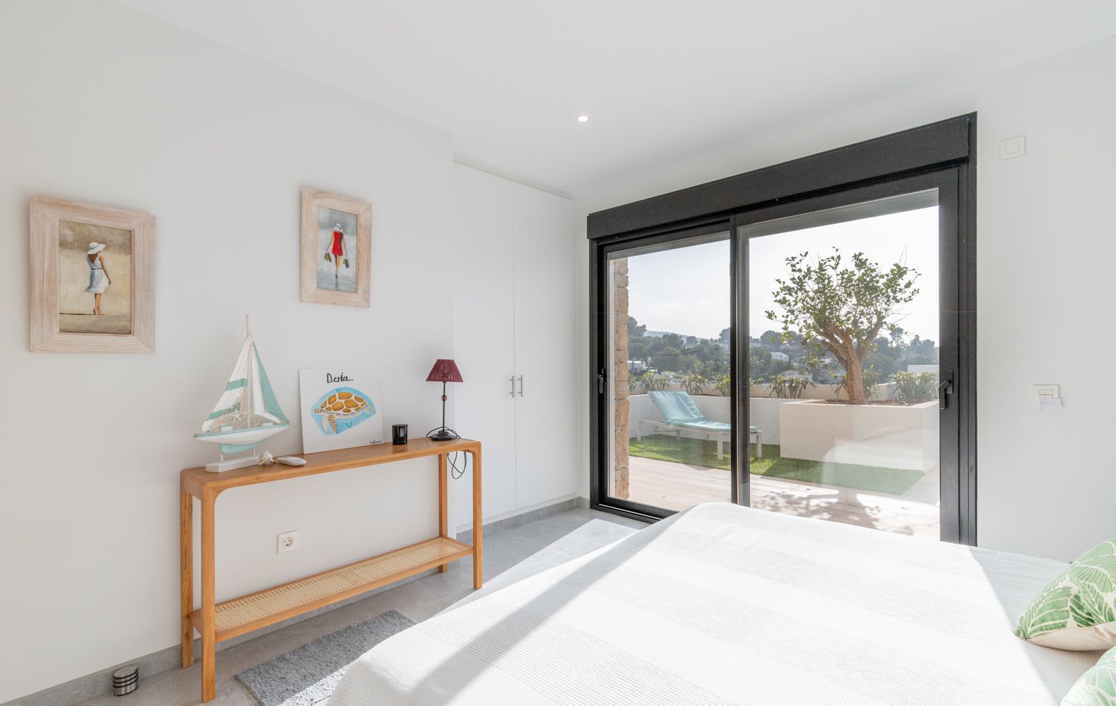 Bright bedroom featuring white built-in wardrobes and sliding glass doors that open onto a private terrace with artificial turf and lounge seating.