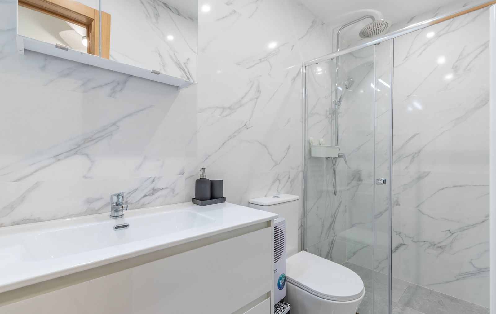 Contemporary bathroom featuring marble-effect porcelain walls, a white vanity with integrated sink, and a walk-in glass shower with chrome fixtures.