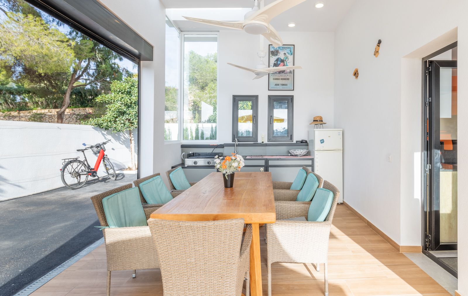 Covered outdoor dining area featuring a summer kitchen, solid wood table, wicker seating, and dual ceiling fans, seamlessly integrated with the exterior patio.