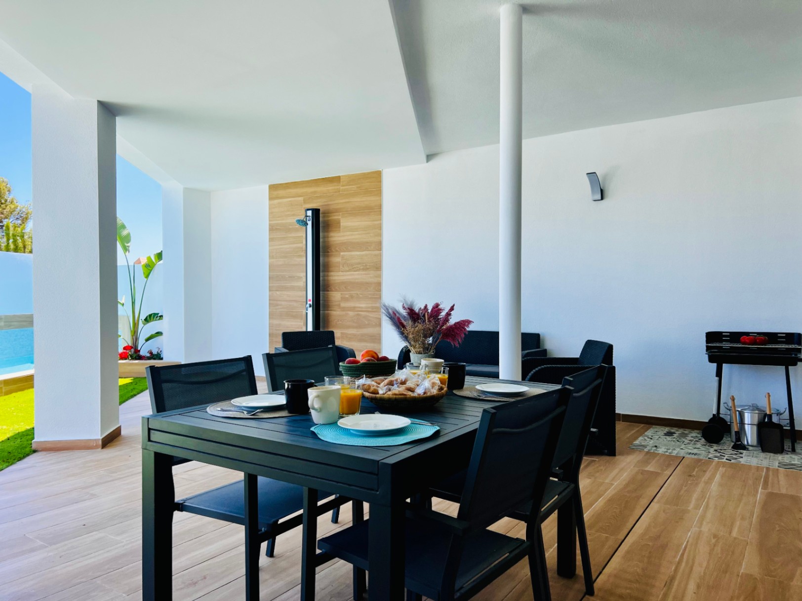 Covered terrace featuring wood-effect porcelain flooring, a modern outdoor dining set, integrated barbecue area, and a sleek outdoor shower.