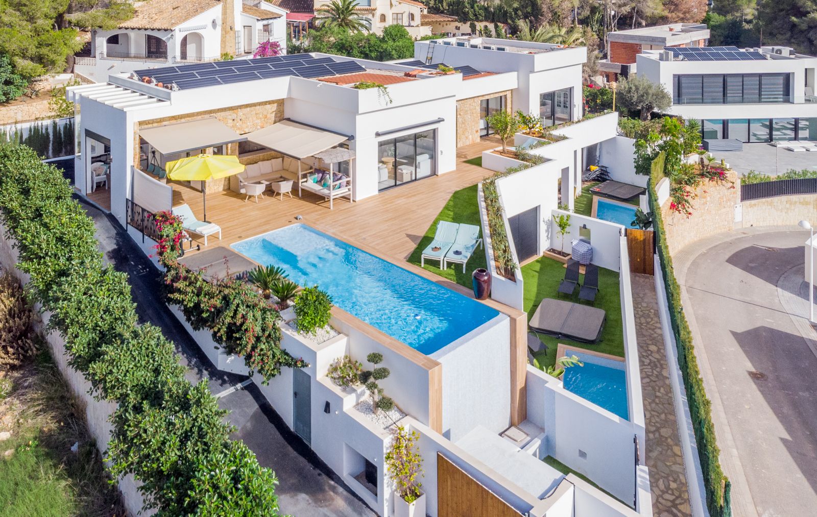 Elevated view of the modern villa featuring an infinity pool, extensive decking, rooftop solar panels, and private outdoor areas for guest apartments.