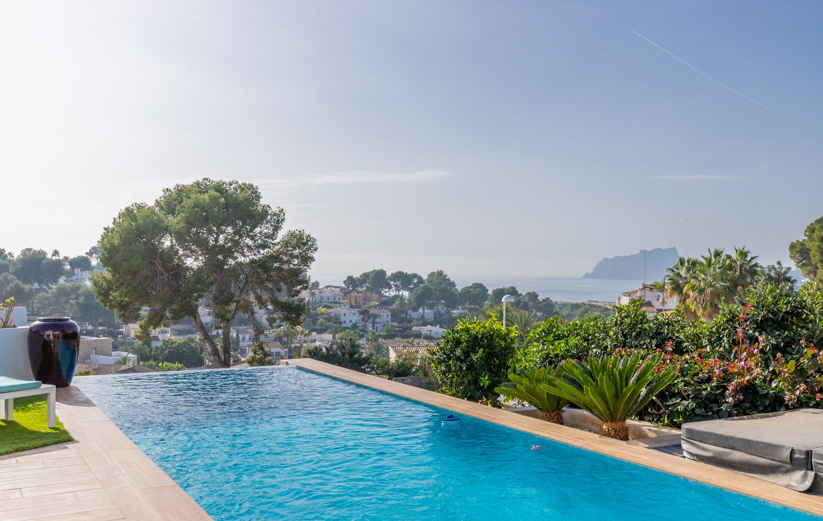 Infinity pool offering panoramic views of the Mediterranean Sea and Peñón de Ifach, featuring a light stone terrace and lush Mediterranean landscaping.