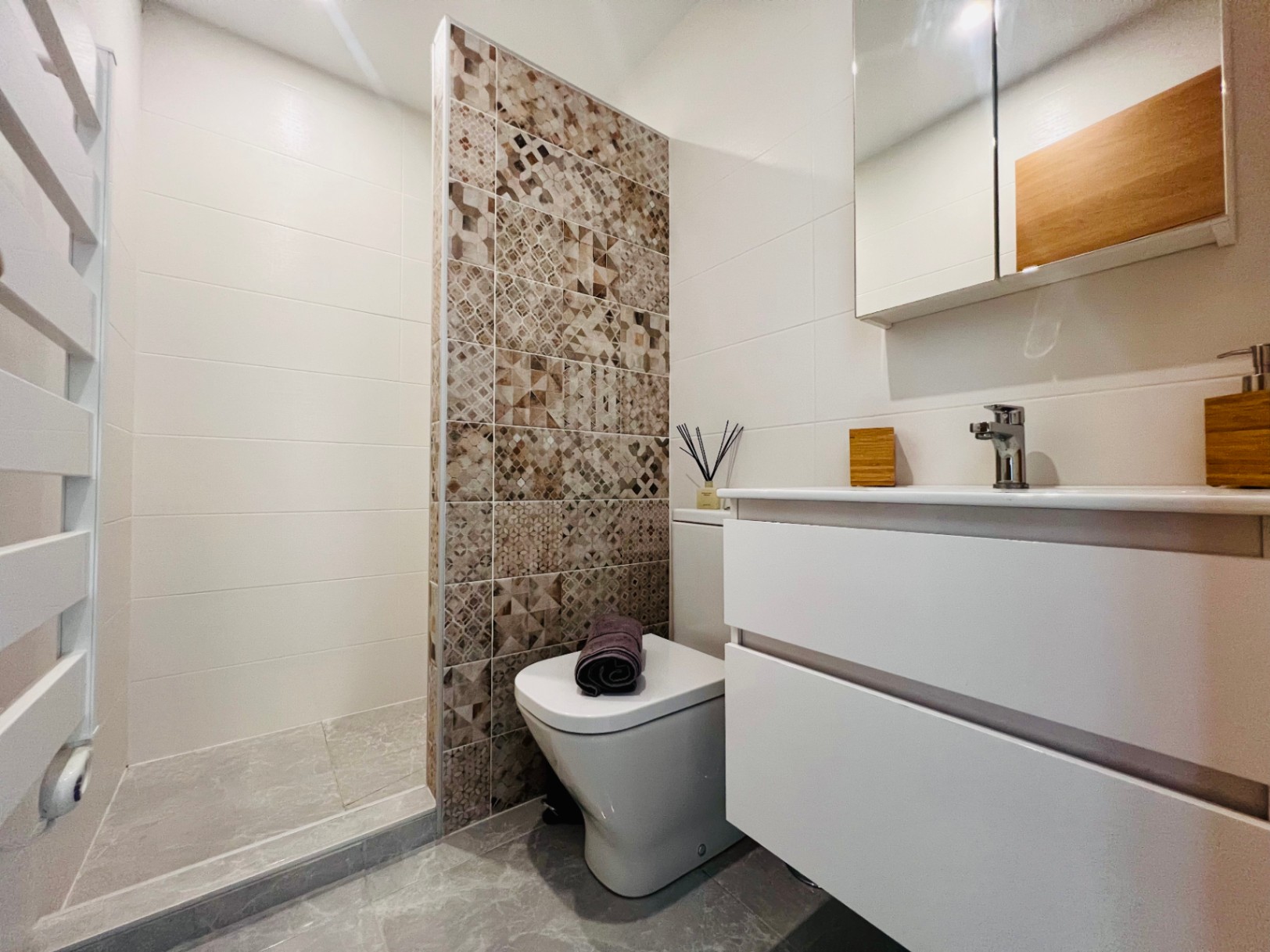 Modern bathroom featuring a walk-in shower with patterned accent tiles, a floating white vanity, and a sleek integrated towel warmer.