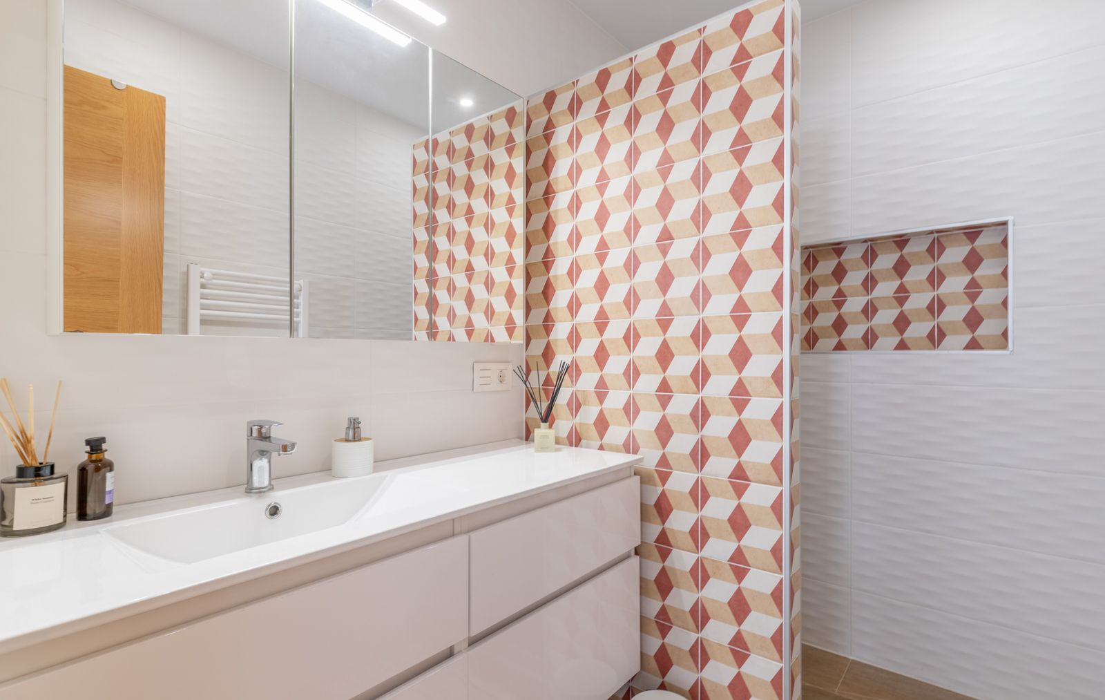 Modern bathroom featuring a white vanity with integrated sink, large mirrored cabinet, and a geometric patterned feature wall with a recessed niche.