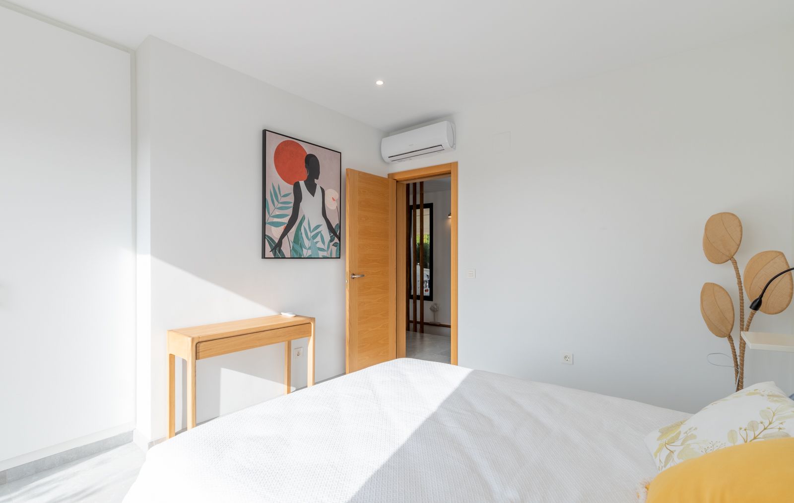 Modern bedroom featuring white walls, a natural wood console table, and split air conditioning. The space is accented by light wood carpentry and contemporary decor.