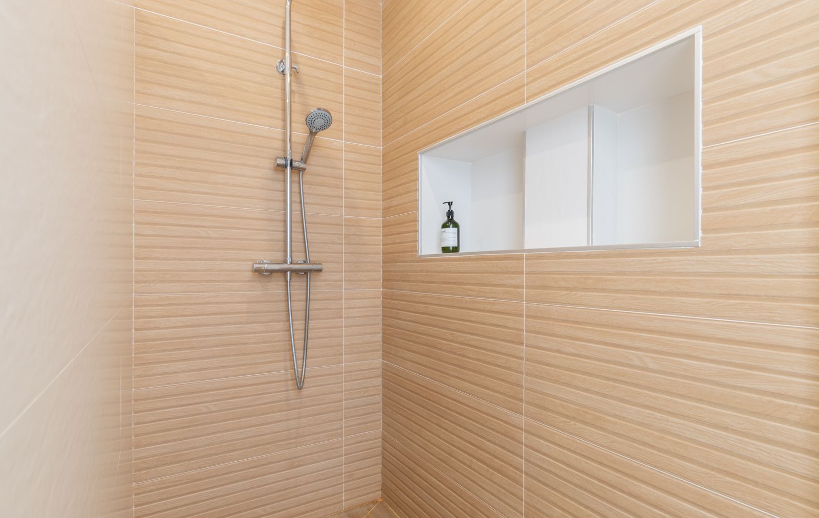 Modern walk-in shower featuring horizontal wood-effect tiling, chrome fixtures, and a recessed built-in wall niche for storage.