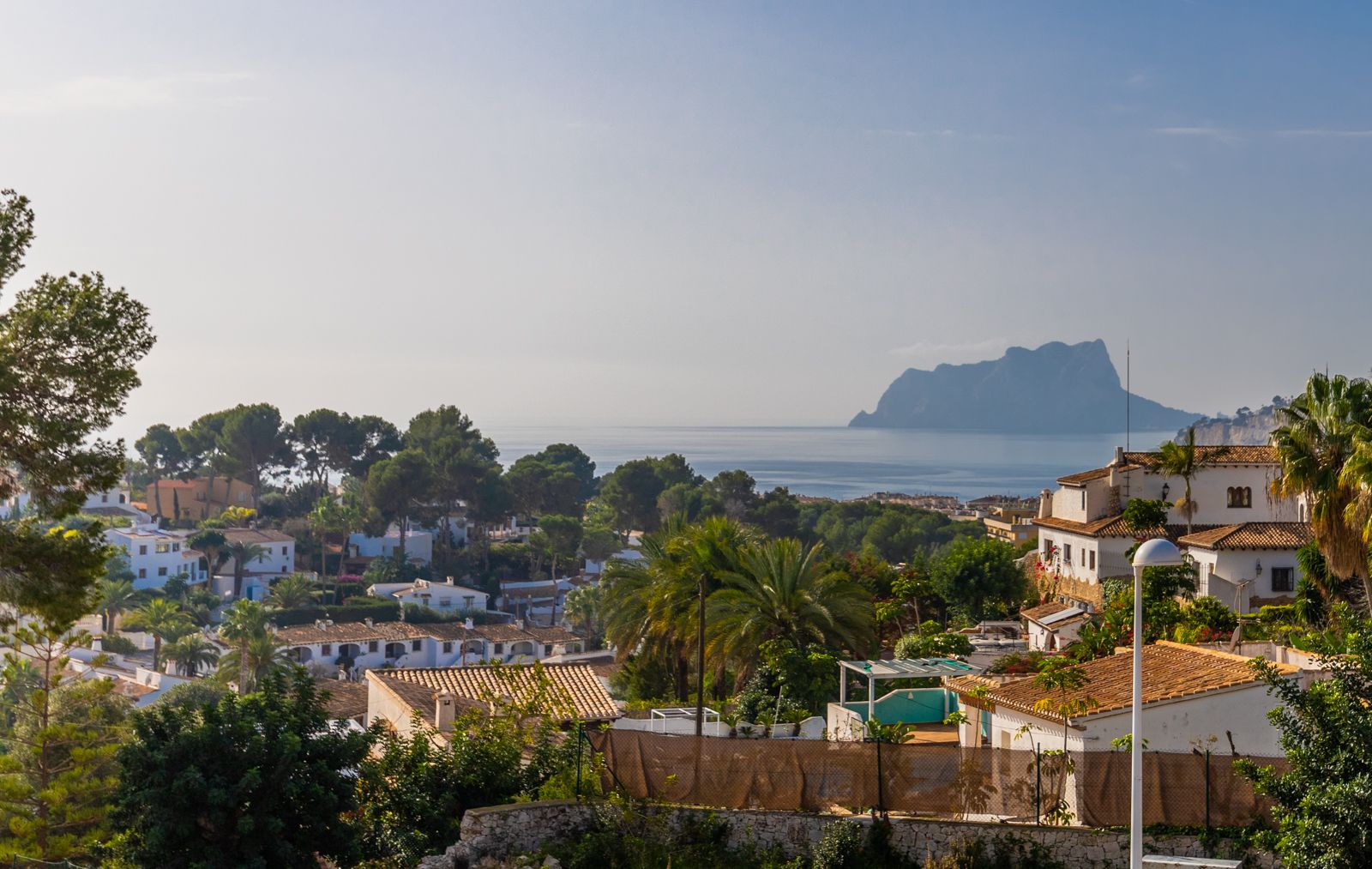 Panoramic views of the Mediterranean Sea and the Peñón de Ifach, overlooking a landscape of traditional white villas and lush palm trees.