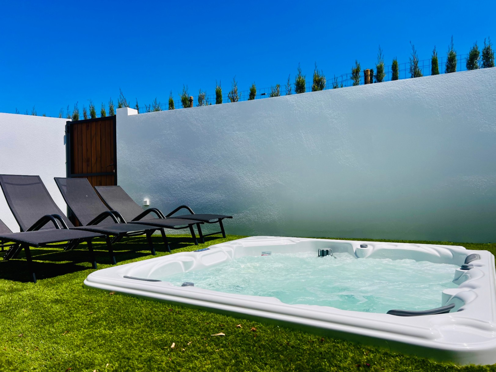 Private hot tub embedded in artificial turf, featuring ergonomic sun loungers and a white perimeter wall for secluded relaxation under the Mediterranean sun.