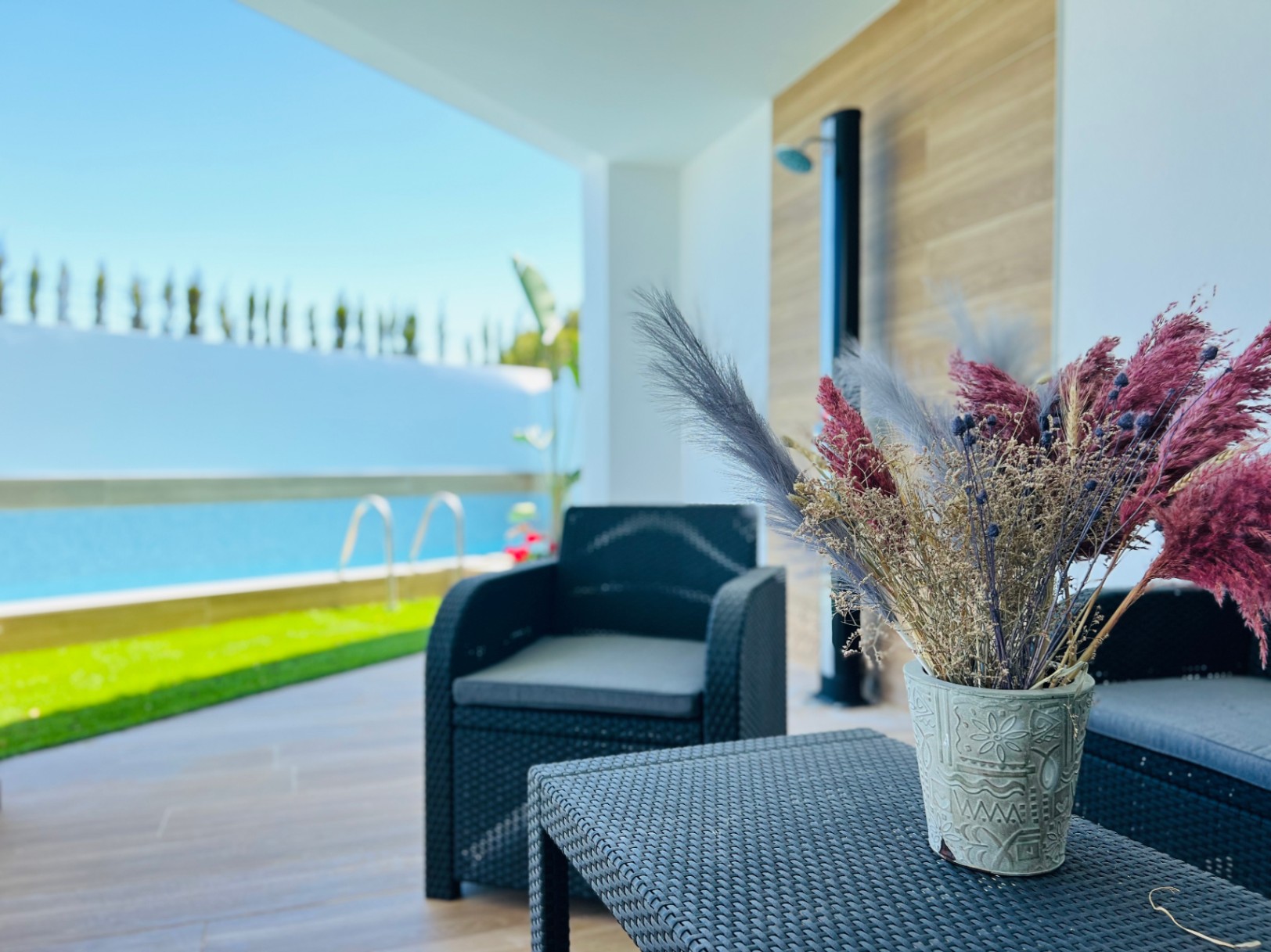 Shaded outdoor lounge featuring dark wicker furniture and a decorative centerpiece, overlooking the private pool and manicured lawn.