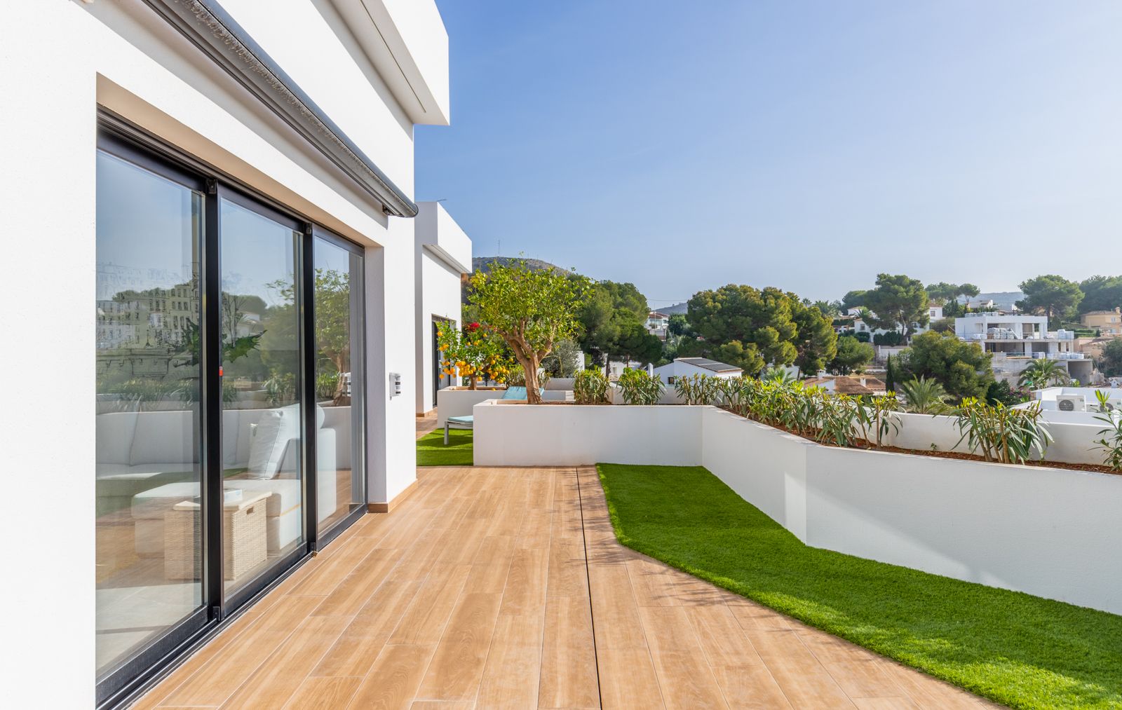 Upper terrace featuring wood-effect porcelain flooring, artificial turf sections, and integrated white planters overlooking the residential area.