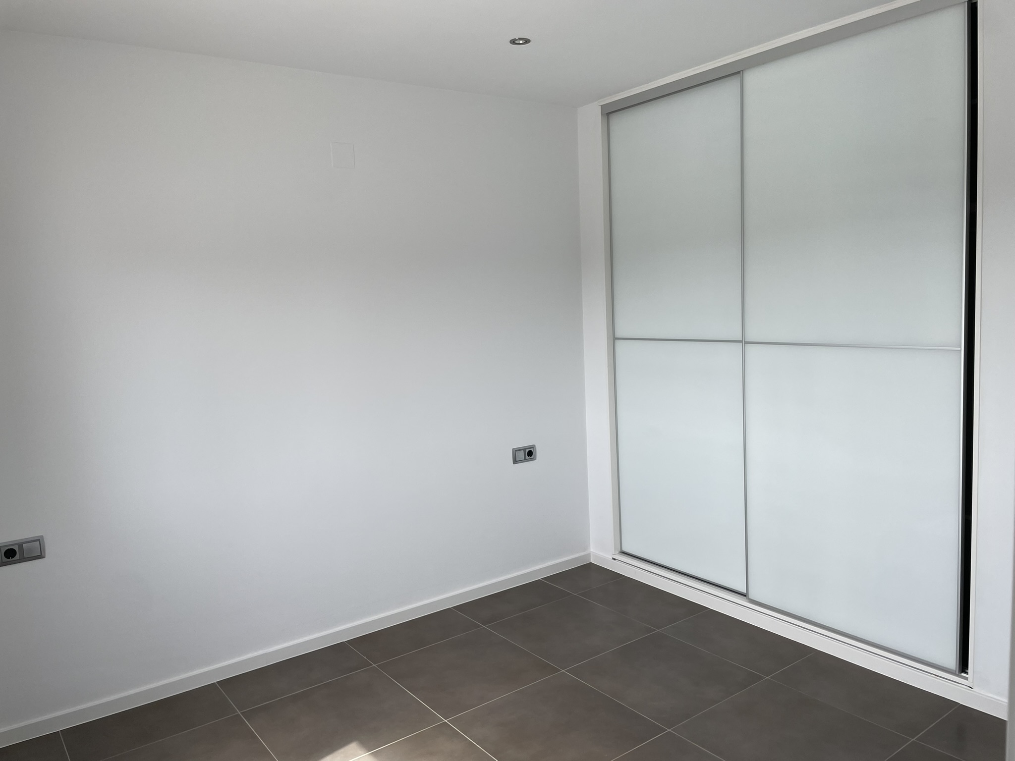Bedroom featuring a built-in wardrobe with white sliding doors, dark porcelain floor tiles, and recessed ceiling lighting.