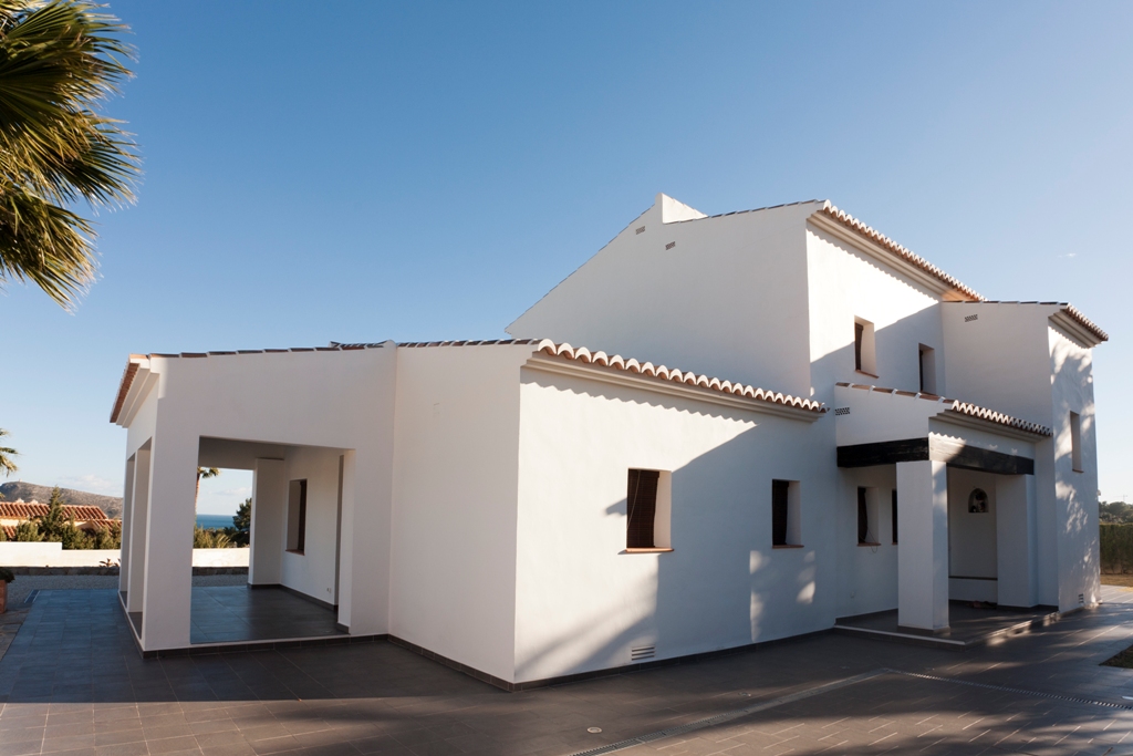 Exterior view of the Mediterranean villa featuring white facades, terracotta roof tiles, and expansive tiled terraces leading to a covered porch with sea views.