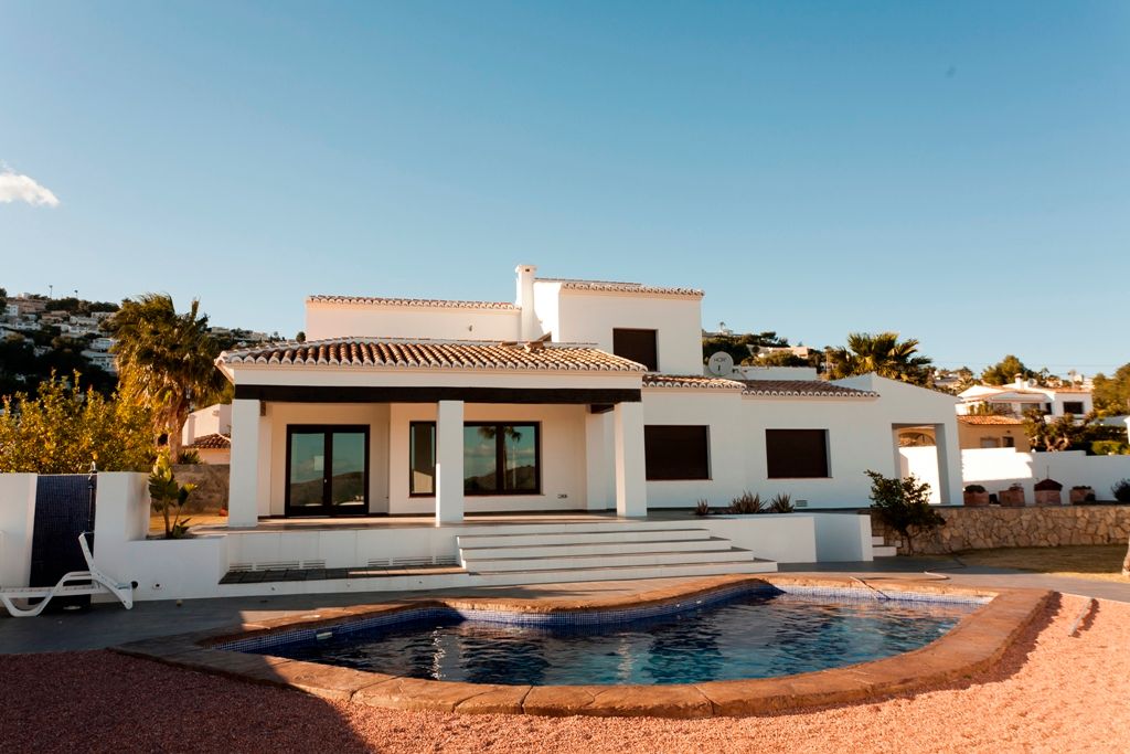 Exterior view showing the irregular-shaped pool, covered terrace with dark wooden beams, and white Mediterranean architecture on a level plot.