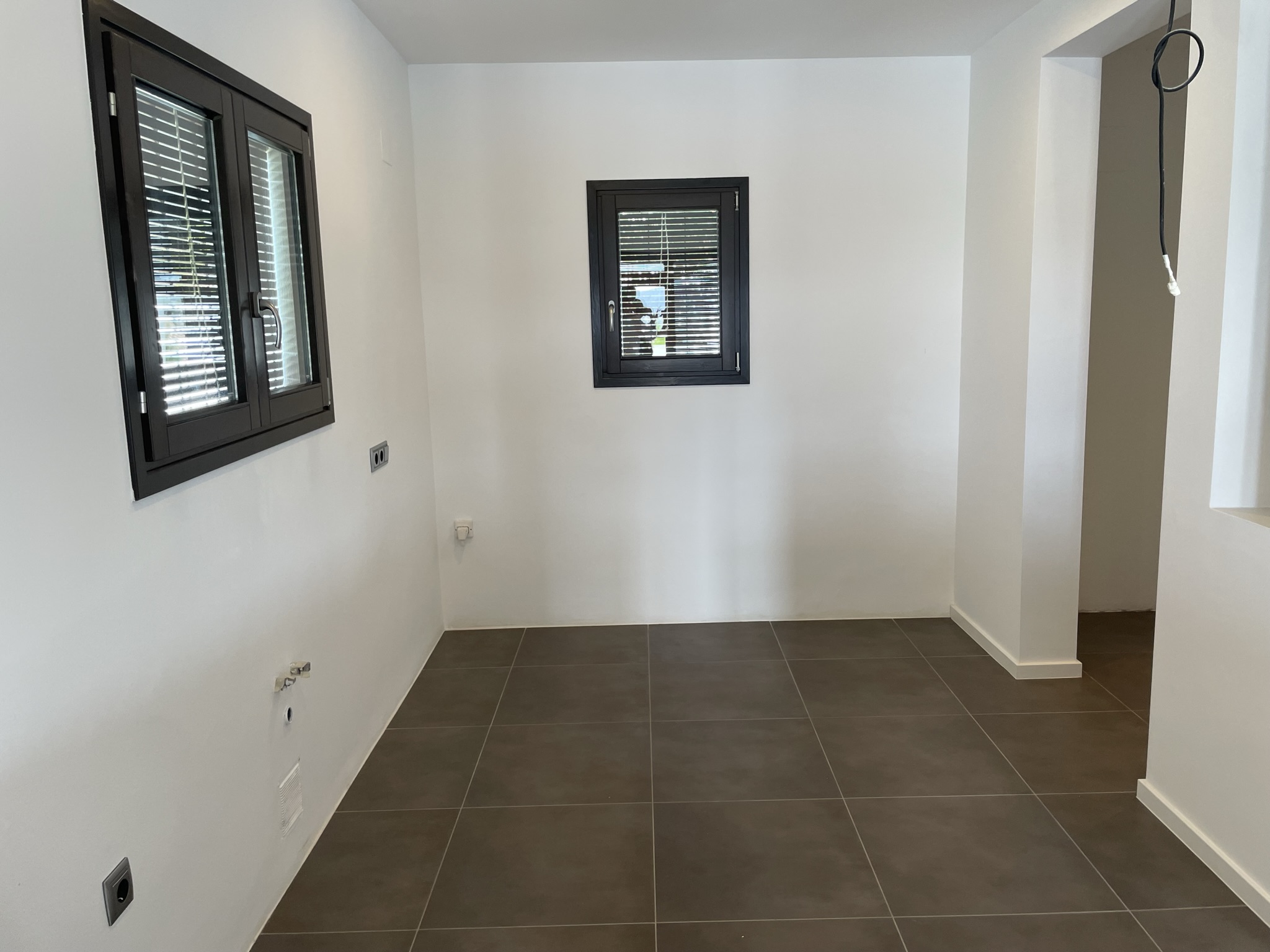 Interior space featuring plumbing and electrical pre-installations, dark porcelain tile flooring, and aluminum windows with integrated blinds.