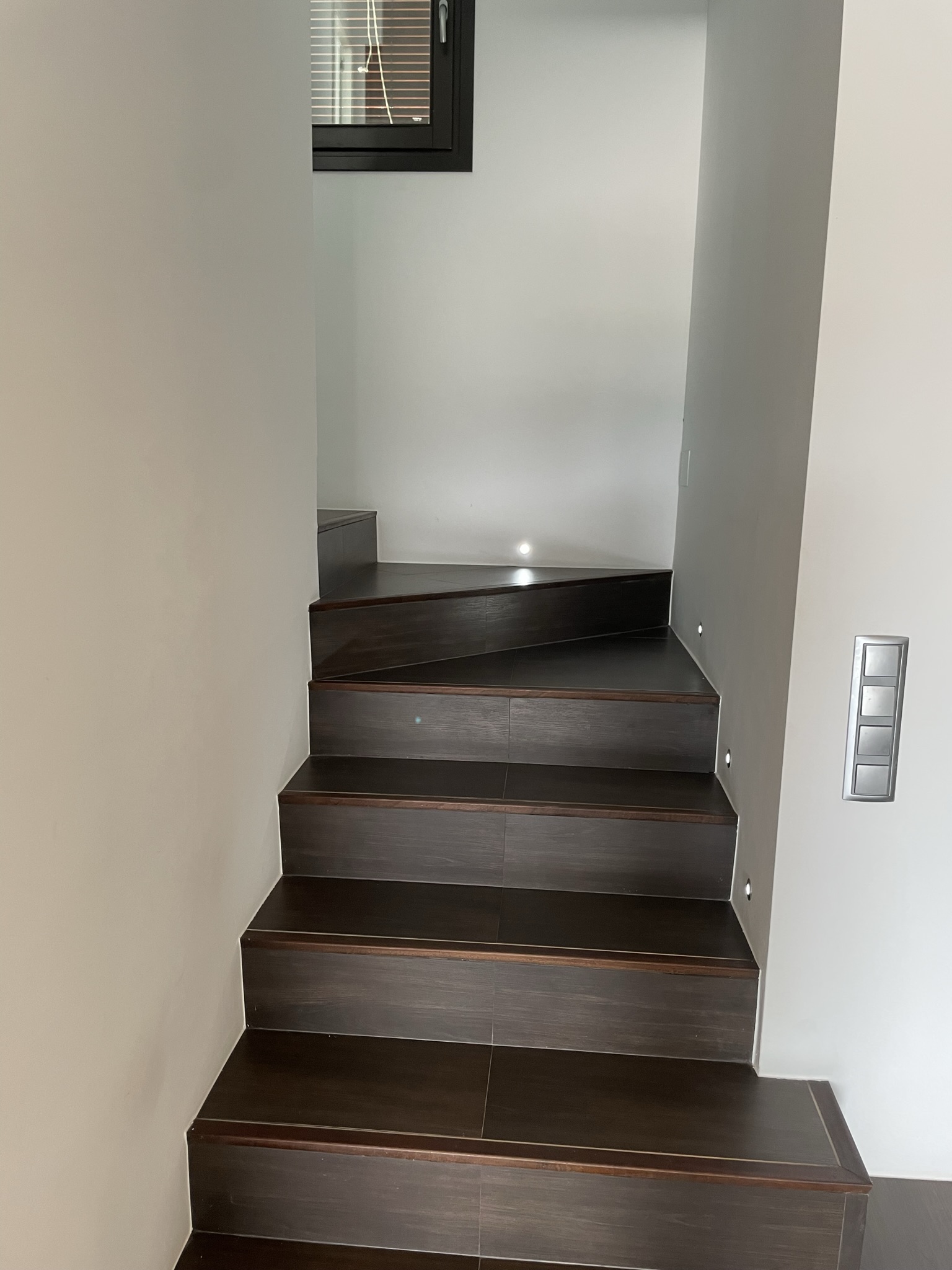 Interior staircase featuring dark wood-effect steps with integrated recessed LED wall lighting and a modern minimalist design.