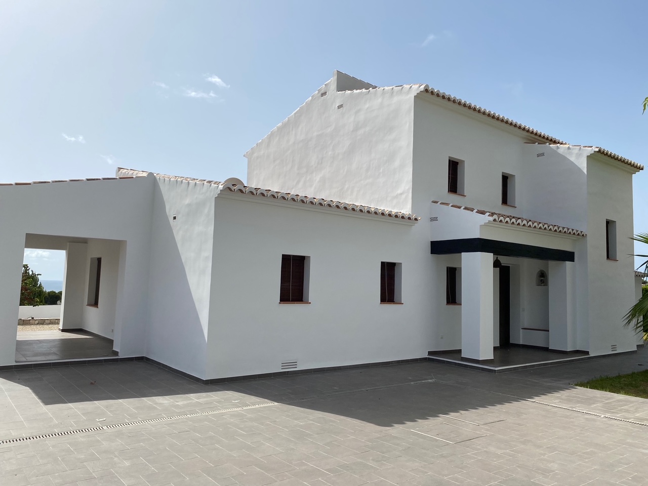 Mediterranean exterior featuring white plastered walls, terracotta roof tiles, and a large grey tiled patio with integrated drainage systems.