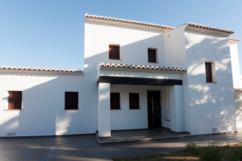 Mediterranean facade featuring white stucco walls, dark wood-effect window frames, and a traditional terracotta tile roof over a shaded porch entrance.