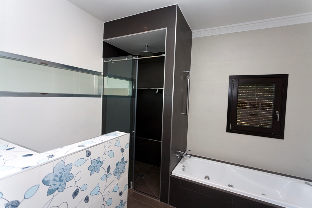 Modern bathroom with a built-in bathtub and separate walk-in shower. Features dark chocolate tiling, a decorative floral partition, and a rain shower head.