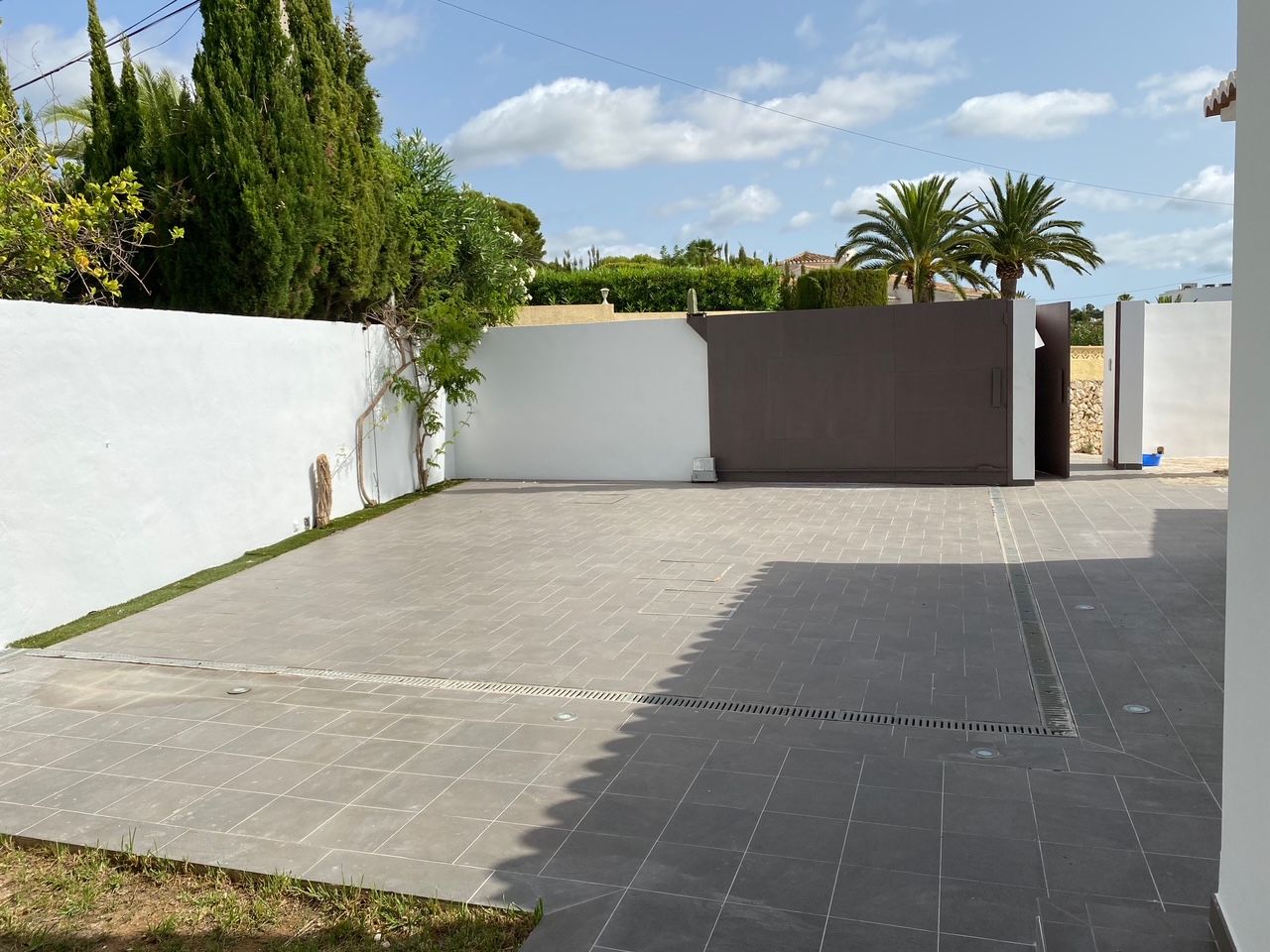 Private parking area featuring grey tiled flooring, a motorized sliding vehicle gate, and independent pedestrian access, enclosed by white walls.