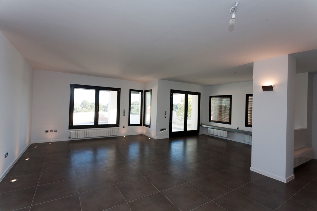 Spacious living area featuring dark porcelain flooring, recessed floor lighting, and wall-mounted radiators. Large dark-framed windows provide ample natural light.