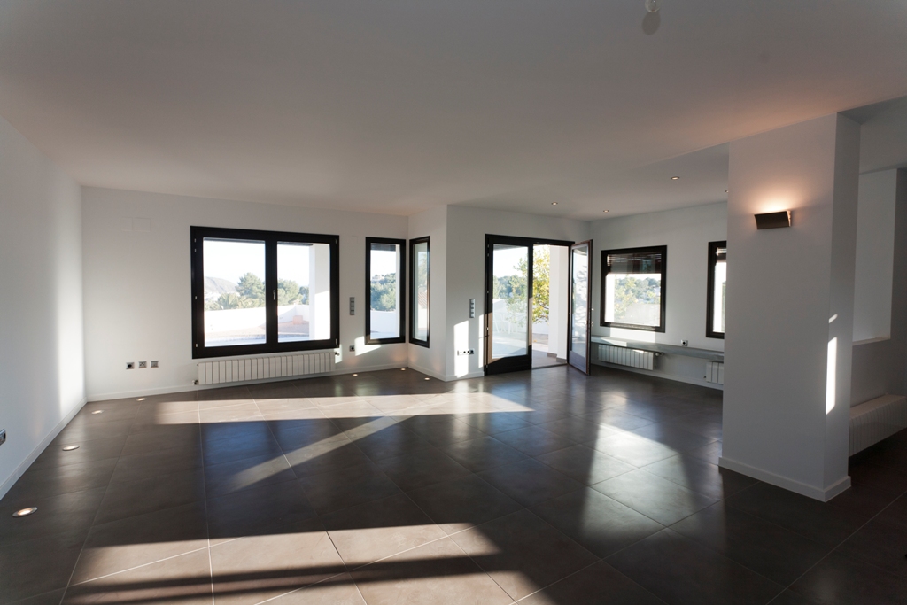 Spacious living area featuring dark tiled flooring, recessed floor lighting, and multiple windows with dark frames providing ample natural light and terrace access.