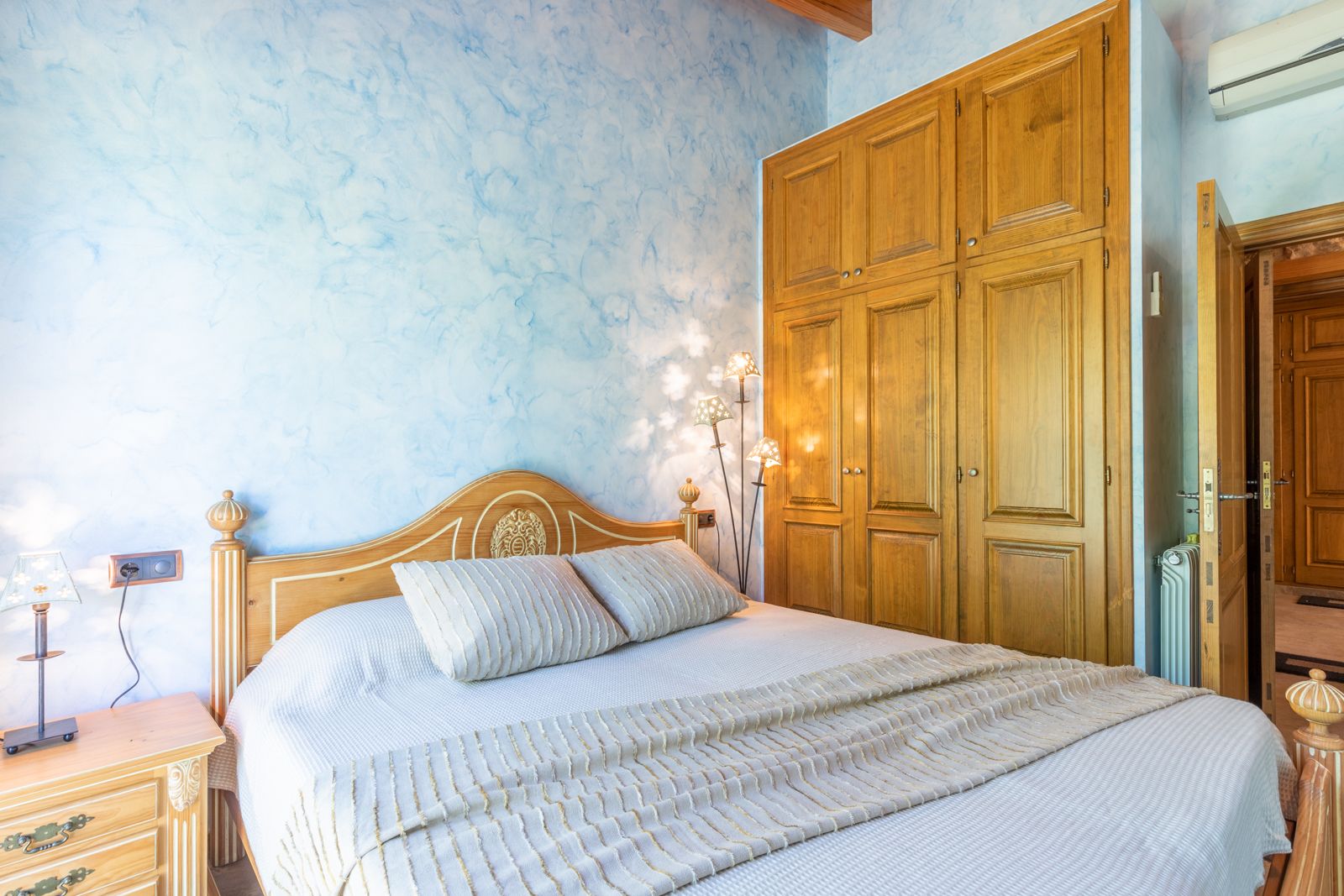 Bedroom featuring a textured blue wall, light wood bed frame, and a built-in wooden wardrobe.