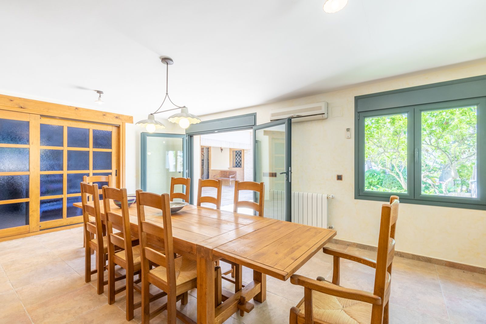 Bright dining room with solid wood table and matching chairs, terrace access, and window overlooking the garden.