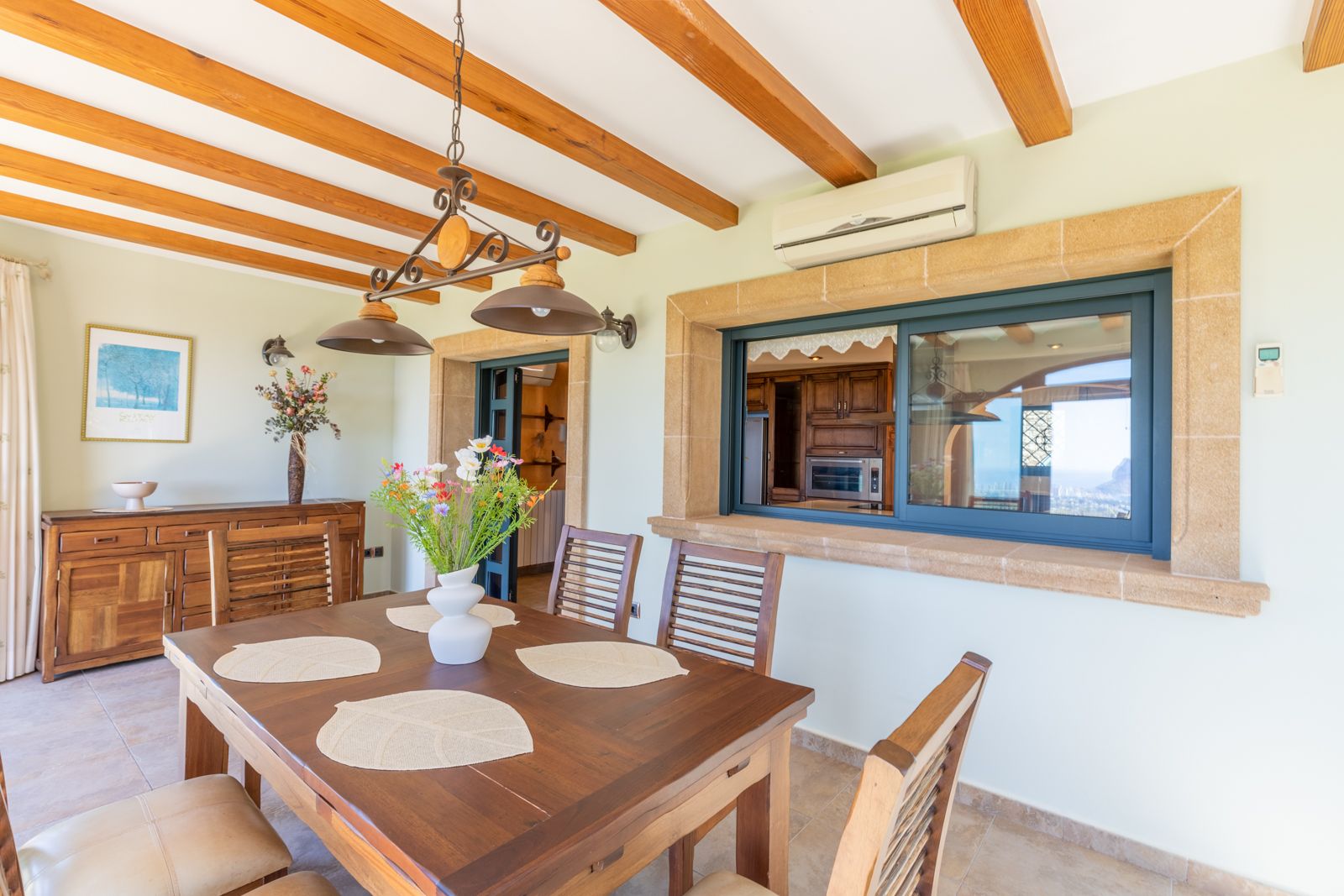 Bright dining room with wooden beams and a view into the equipped kitchen.