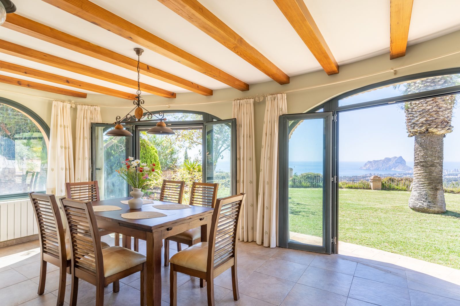 Bright dining room with wooden beams and views of the garden and the Mediterranean Sea.