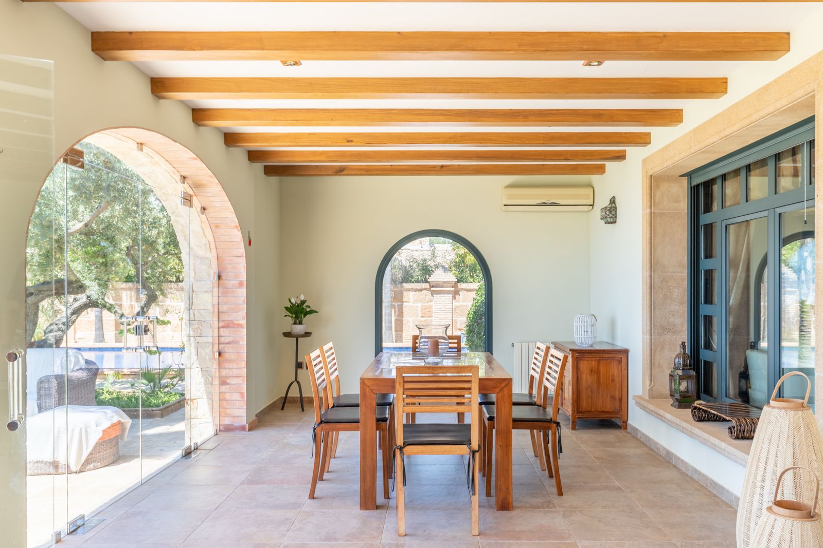 Bright dining room with wooden table and access to the garden and pool through brick arches.