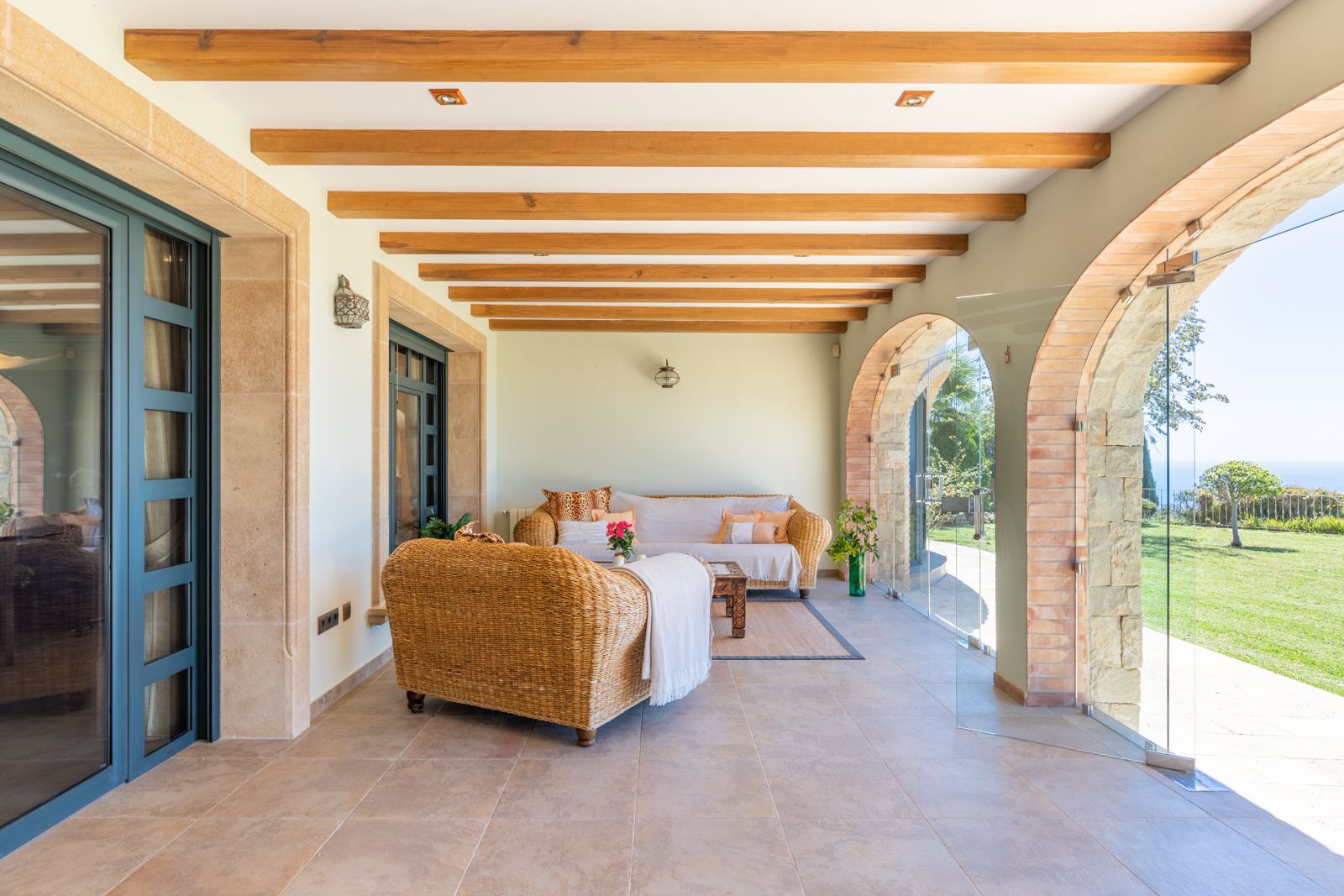 Covered porch with wood beams, stone arches, and views of the garden and sea.