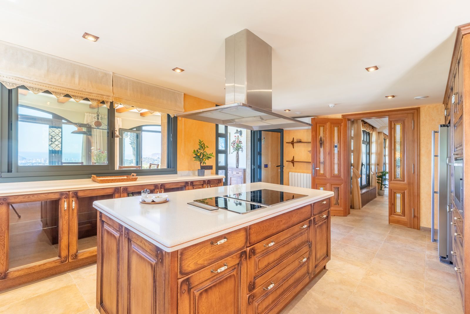 Kitchen with a central wood island, light countertop, and a metal extractor hood. Wide windows with views.