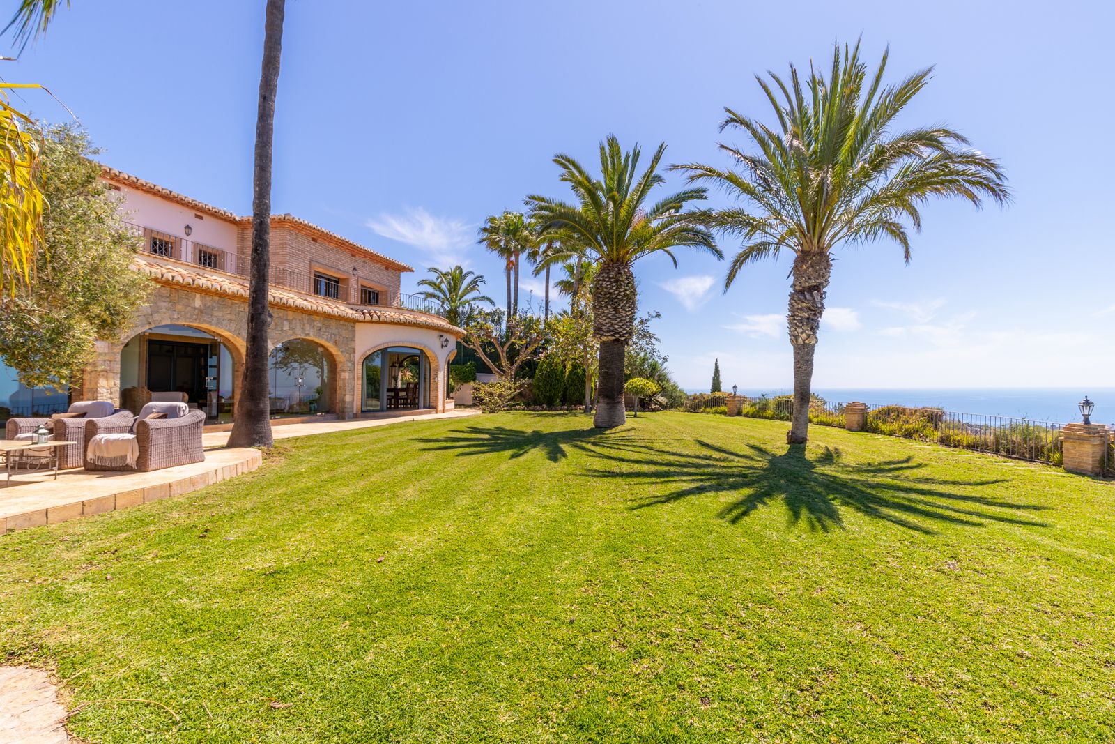 Lawn view of the Mediterranean estate, featuring palm trees and a stone facade with arches.
