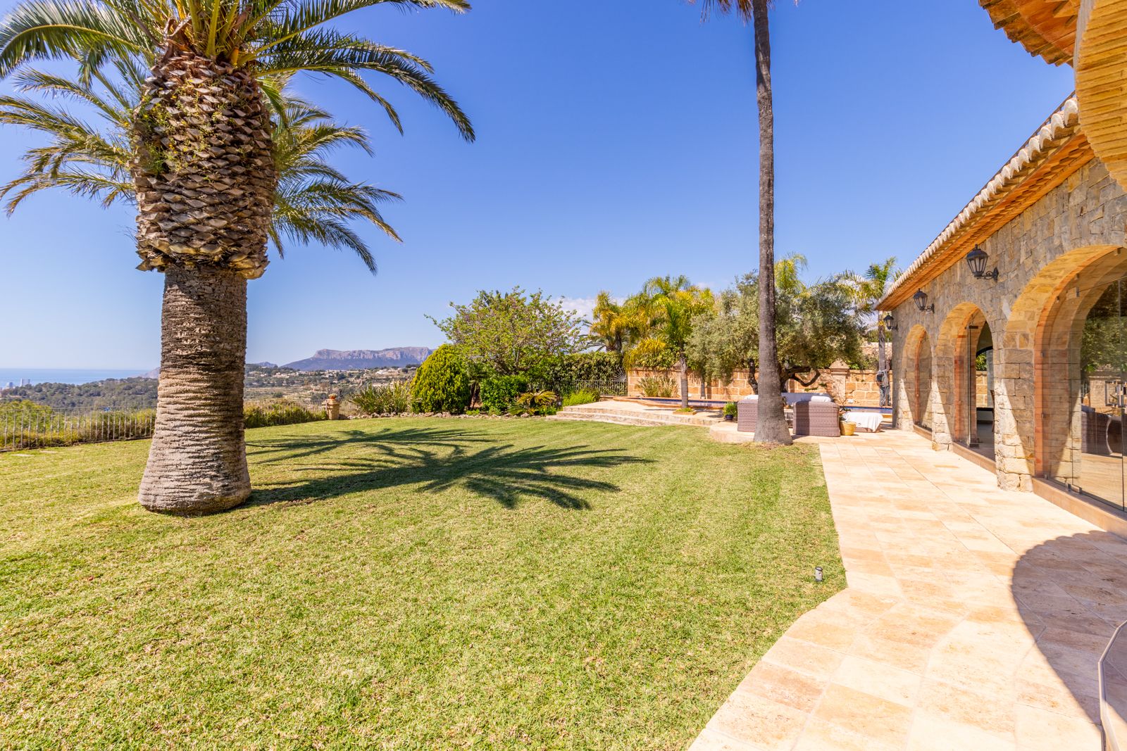 Lawn view with palm trees and stone facade with arches.