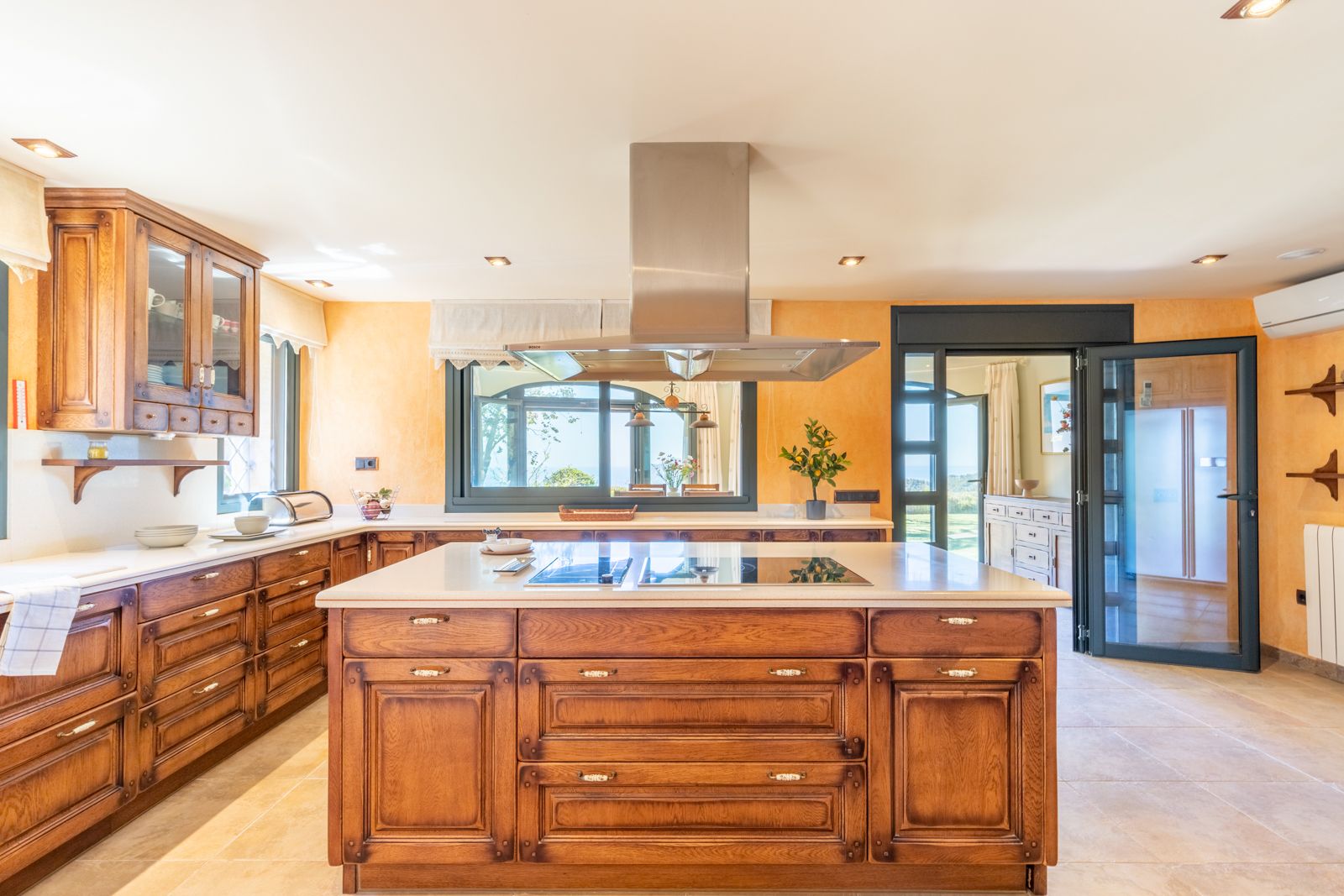 Rustic kitchen featuring a central wood island with light countertop, steel extractor, and outdoor views.